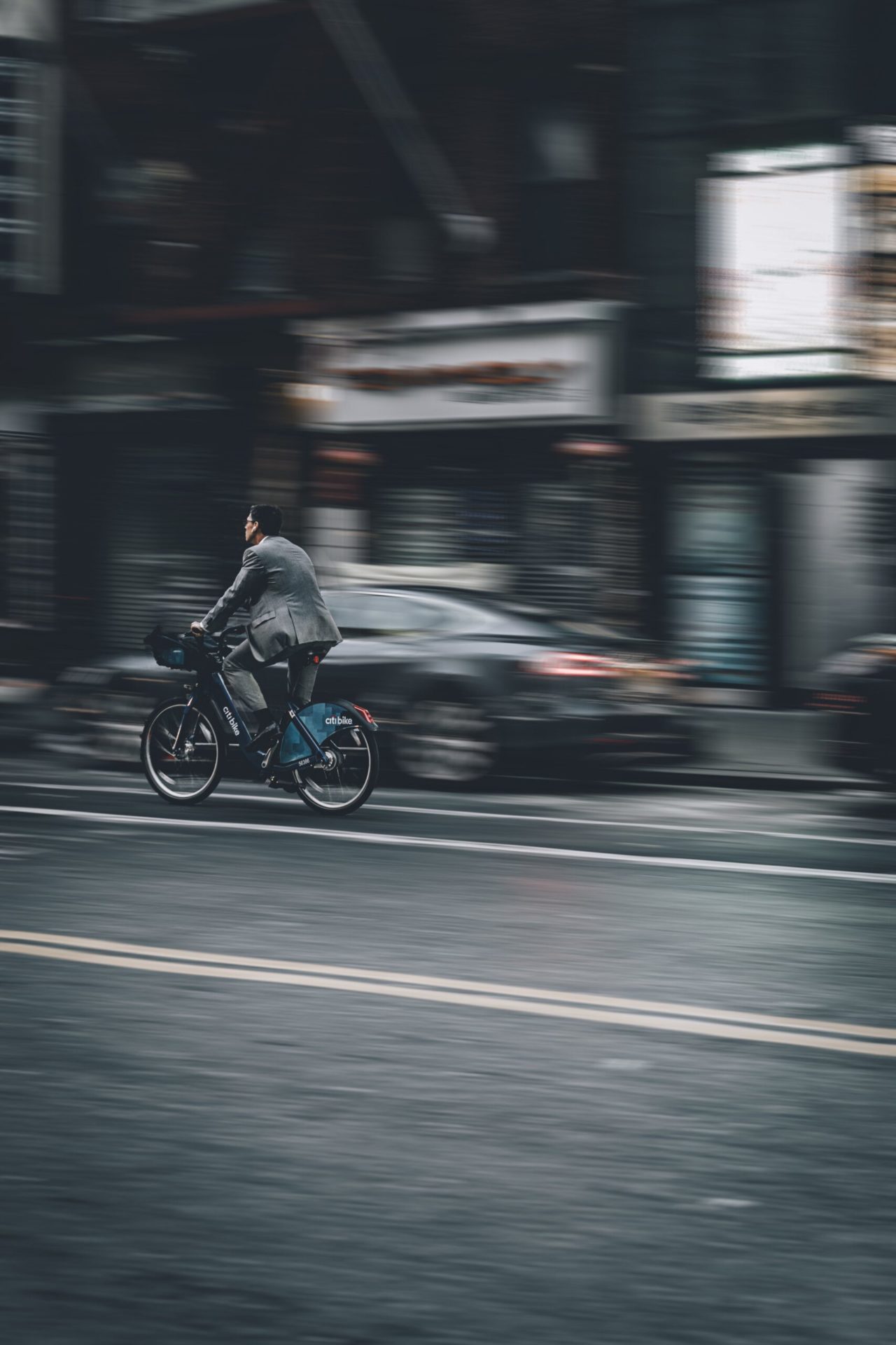 C-level employee in motion passing a car on a bike in a grayish street on the executive search service page
